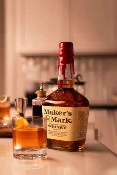 A bottle of Maker's Mark whiskey beside a glass of whiskey